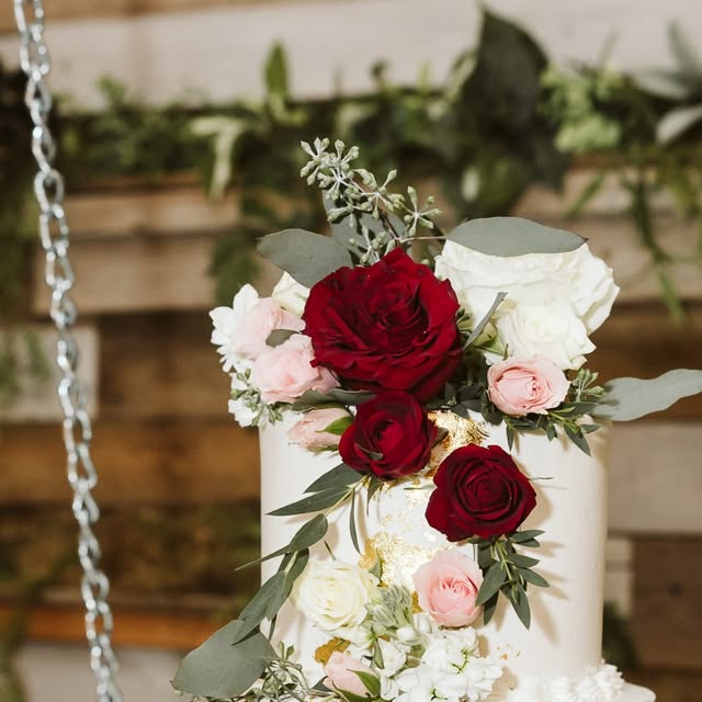 Finished wedding cake with cascading red and blush roses