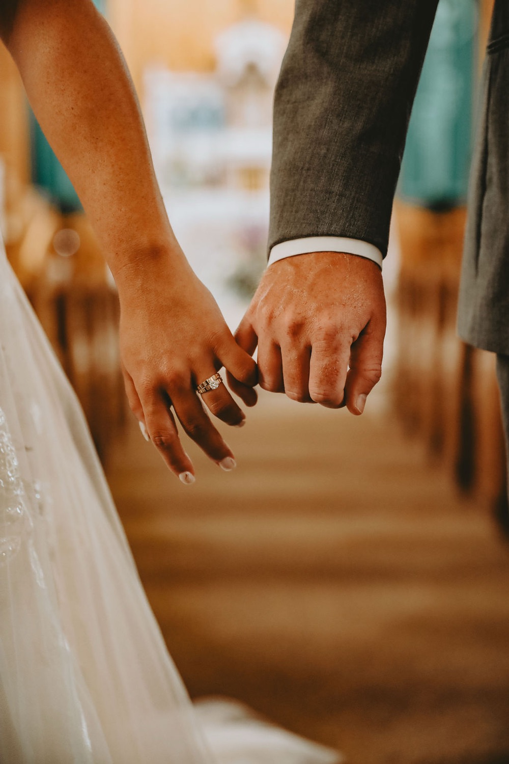 A bride and groom hold hands at their wedding, her ring in view