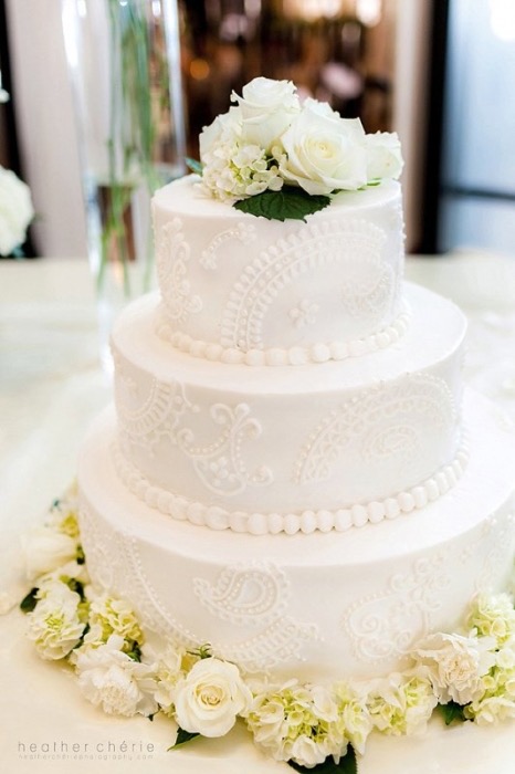 White lace three-tier wedding cake topped with white roses