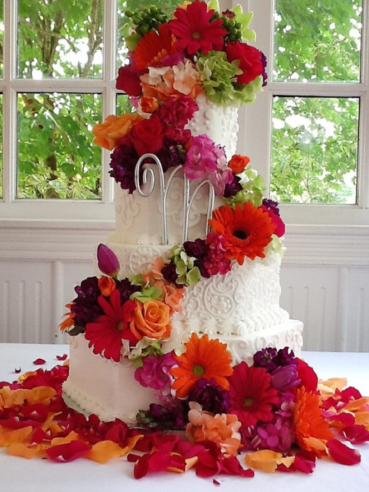 White wedding cake with a cascade of red, orange, and pink flowers