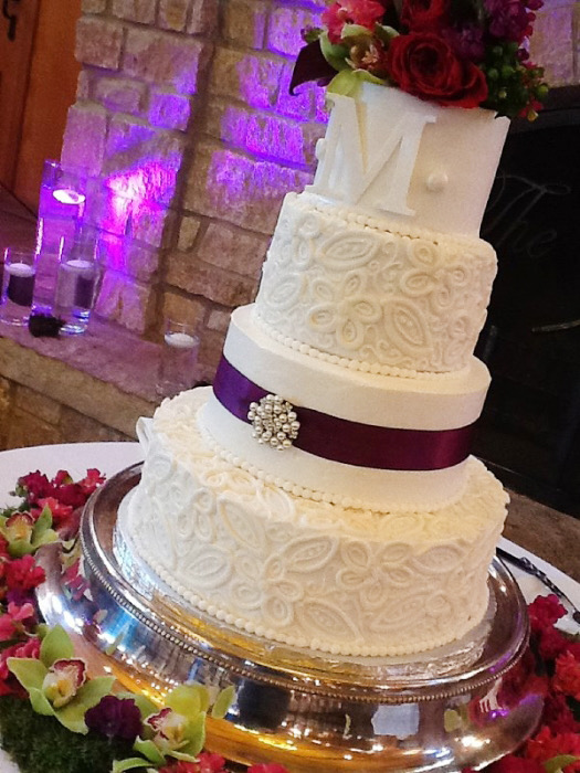 White lace wedding cake with a deep-purple ribbon and roses