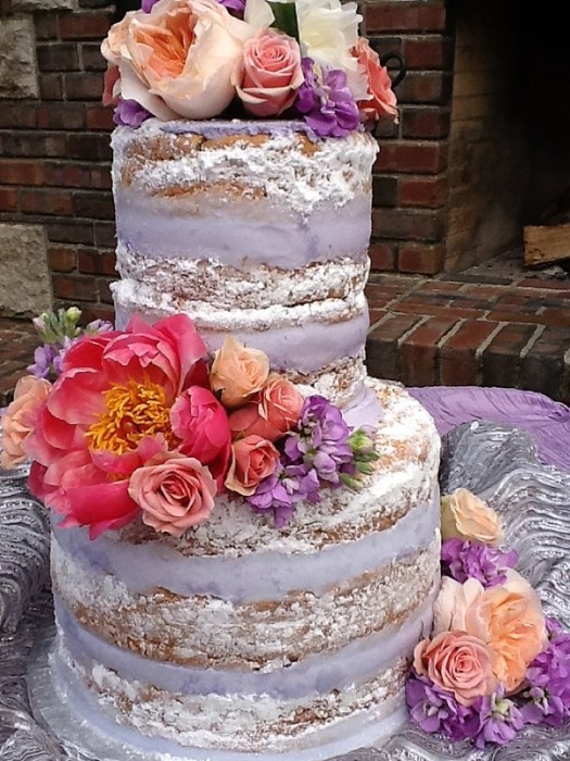 Semi-naked wedding cake topped with bright coral and purple florals