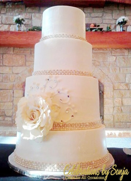 Elegant white wedding cake with a single cream rose by a stone fireplace