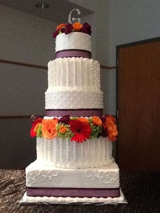 White wedding cake with orange gerbera daisies and a purple ribbon